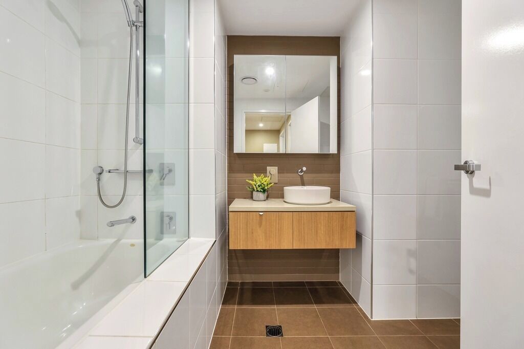 A modern bathroom with a glass-enclosed shower, a white bathtub, a wooden vanity with a sink, and a mirror above the vanity.