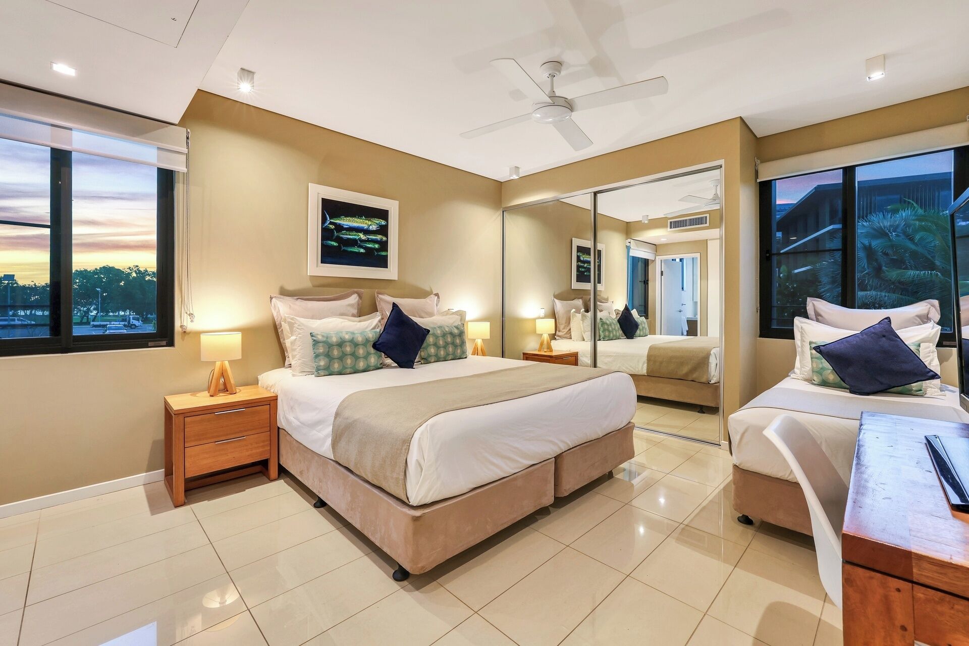A modern hotel room with a large bed, bedside tables, a desk, and a large mirror.