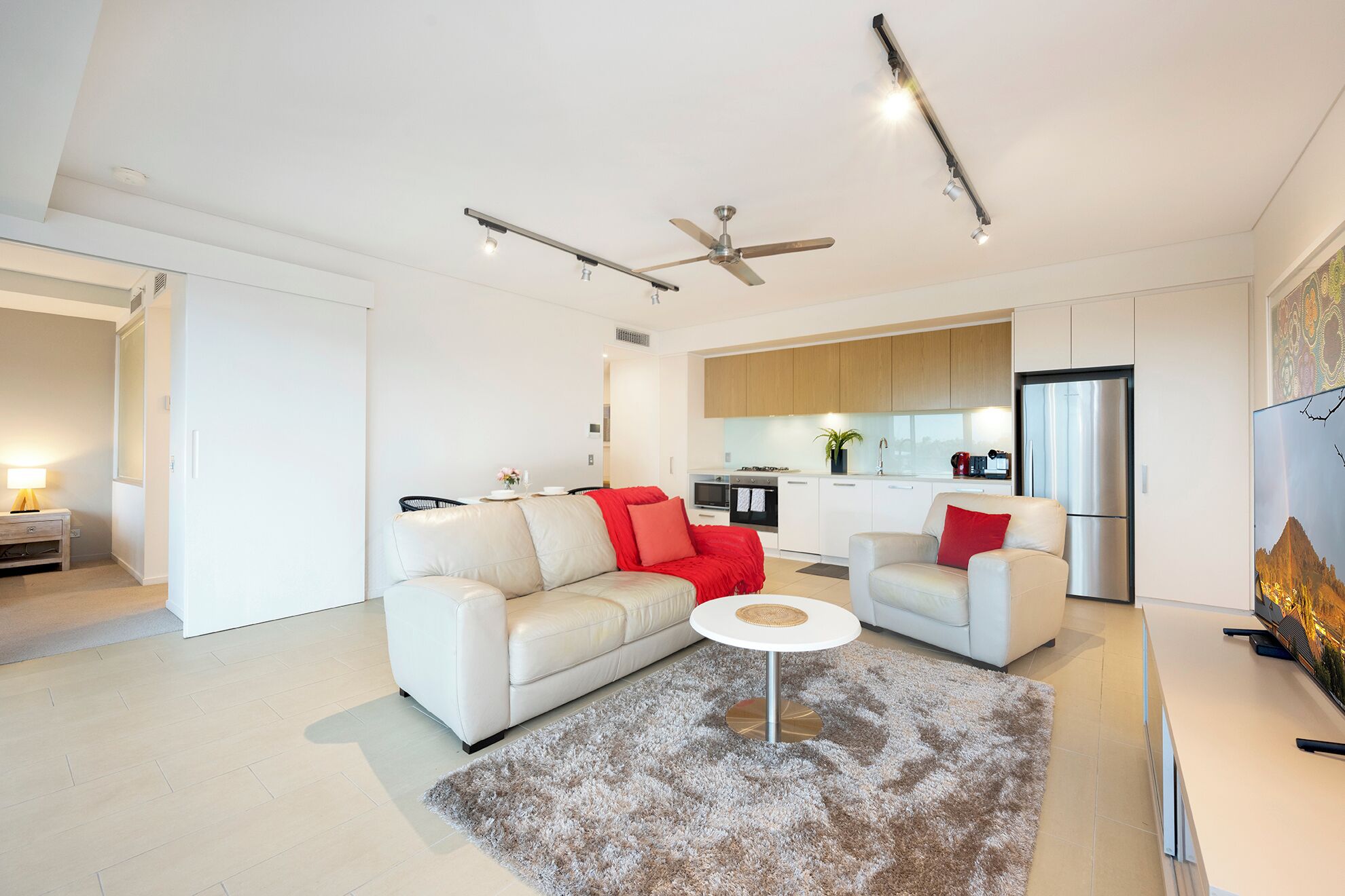 A modern living room with two white sofas, a round coffee table, and a ceiling fan.