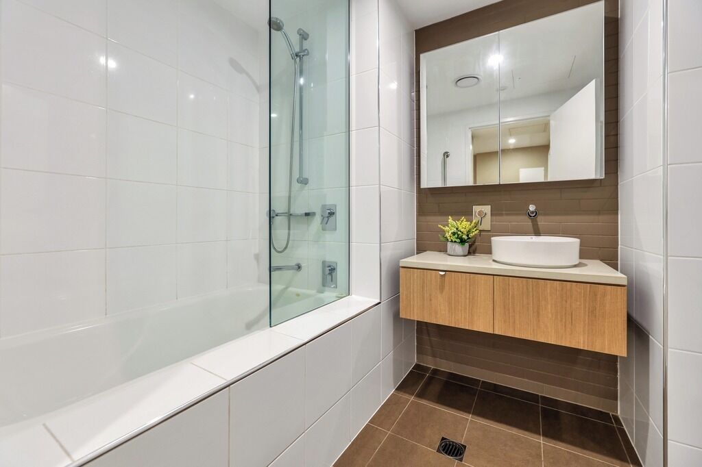 Une salle de bain moderne avec une douche à parois de verre, un meuble-lavabo en bois avec un lavabo blanc et un grand miroir au-dessus du meuble.