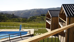 Zona de piscina con terraza de madera y vistas a colinas verdes al fondo.