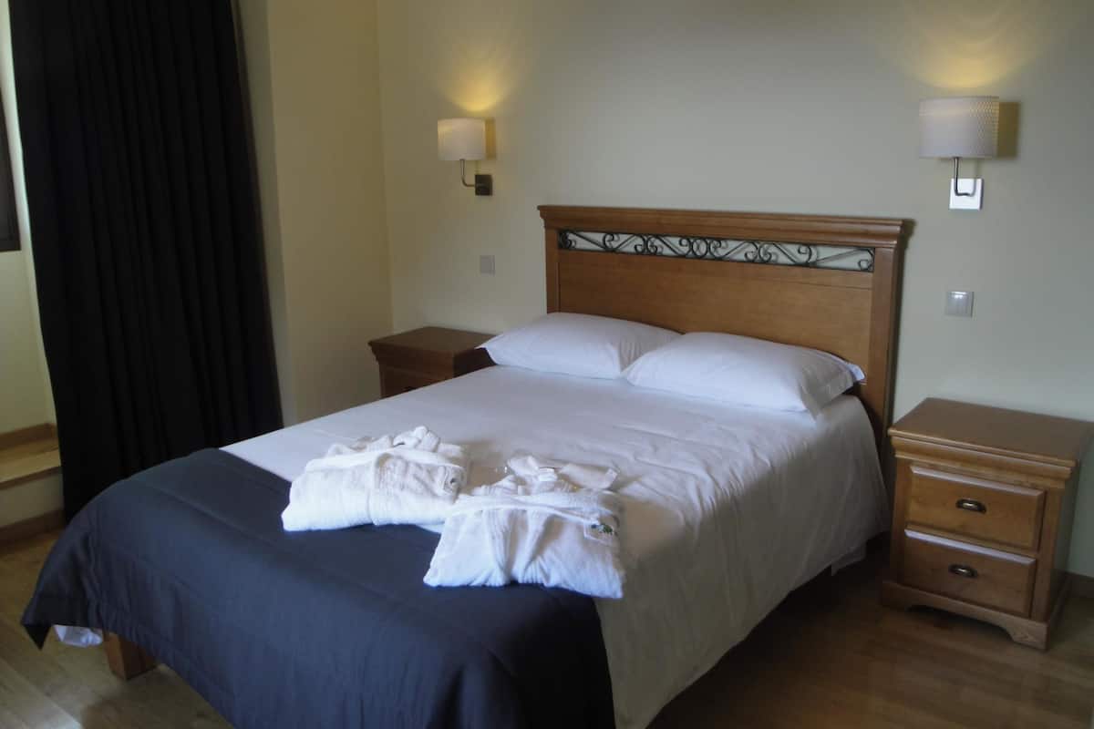Una cama bien hecha con sábanas blancas y una colcha azul oscuro, dos mesitas de noche con lámparas, y un cabecero de madera con detalles decorativos.