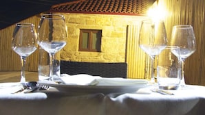 Una mesa preparada con copas de vino y cubiertos, un plato y una vela en una habitación cálidamente iluminada con paredes de madera y techo de tejas.