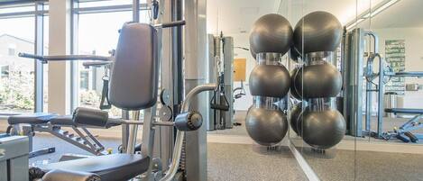Ein Fitnessstudio mit Trainingsgeräten, großen Fenstern und einer Spiegelwand.