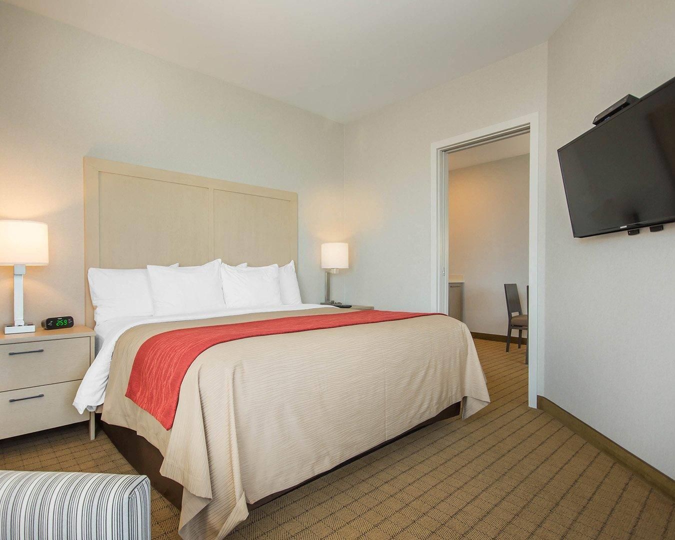 A hotel room with a bed, bedside tables, a TV, and a chair.