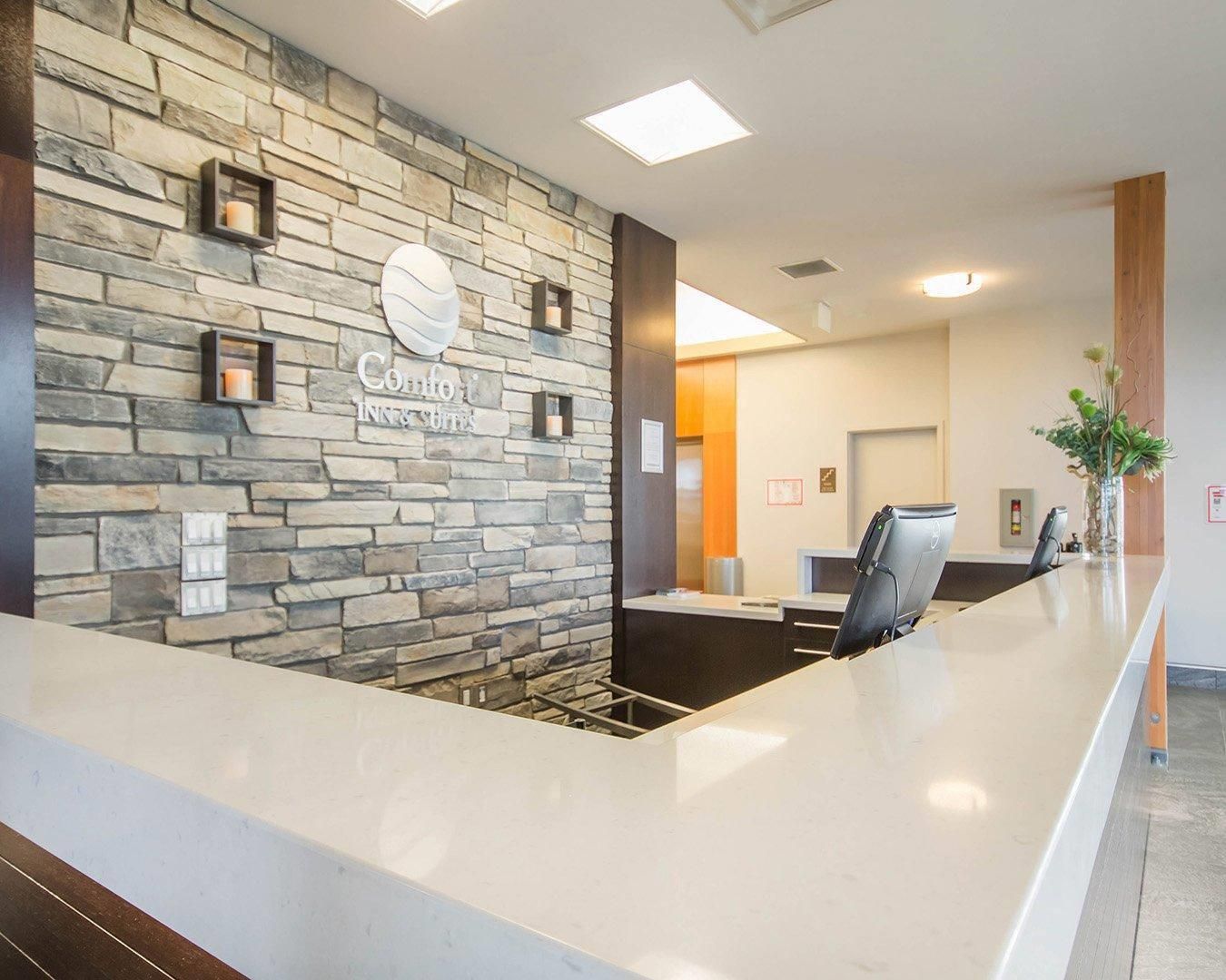 A reception area with a stone wall, a sign for 'Comfort Inn & Suites,' a reception desk, and a seating area with chairs.