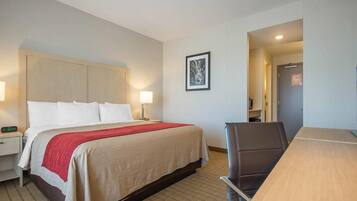 Una habitación de hotel con cama, mesita de noche, lámpara, silla y escritorio.