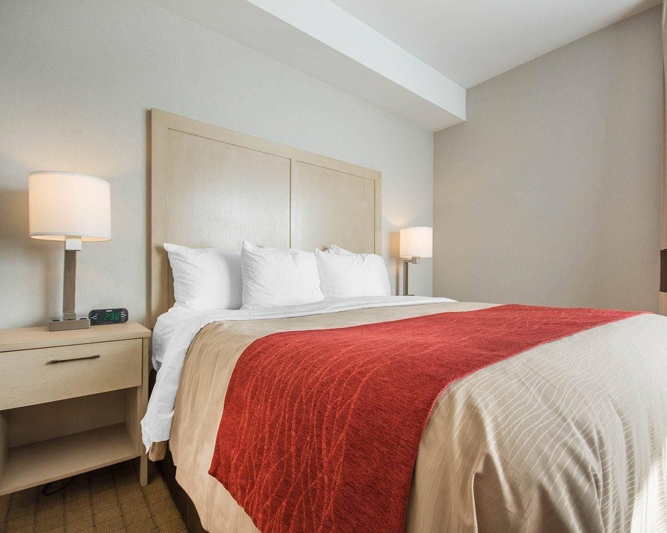 Habitación de hotel con una cama, dos mesitas de noche con lámparas y una manta roja.