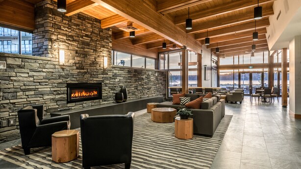 Un vestíbulo espacioso con chimenea de piedra, asientos de cuero, vigas de madera y grandes ventanales que ofrecen vistas.