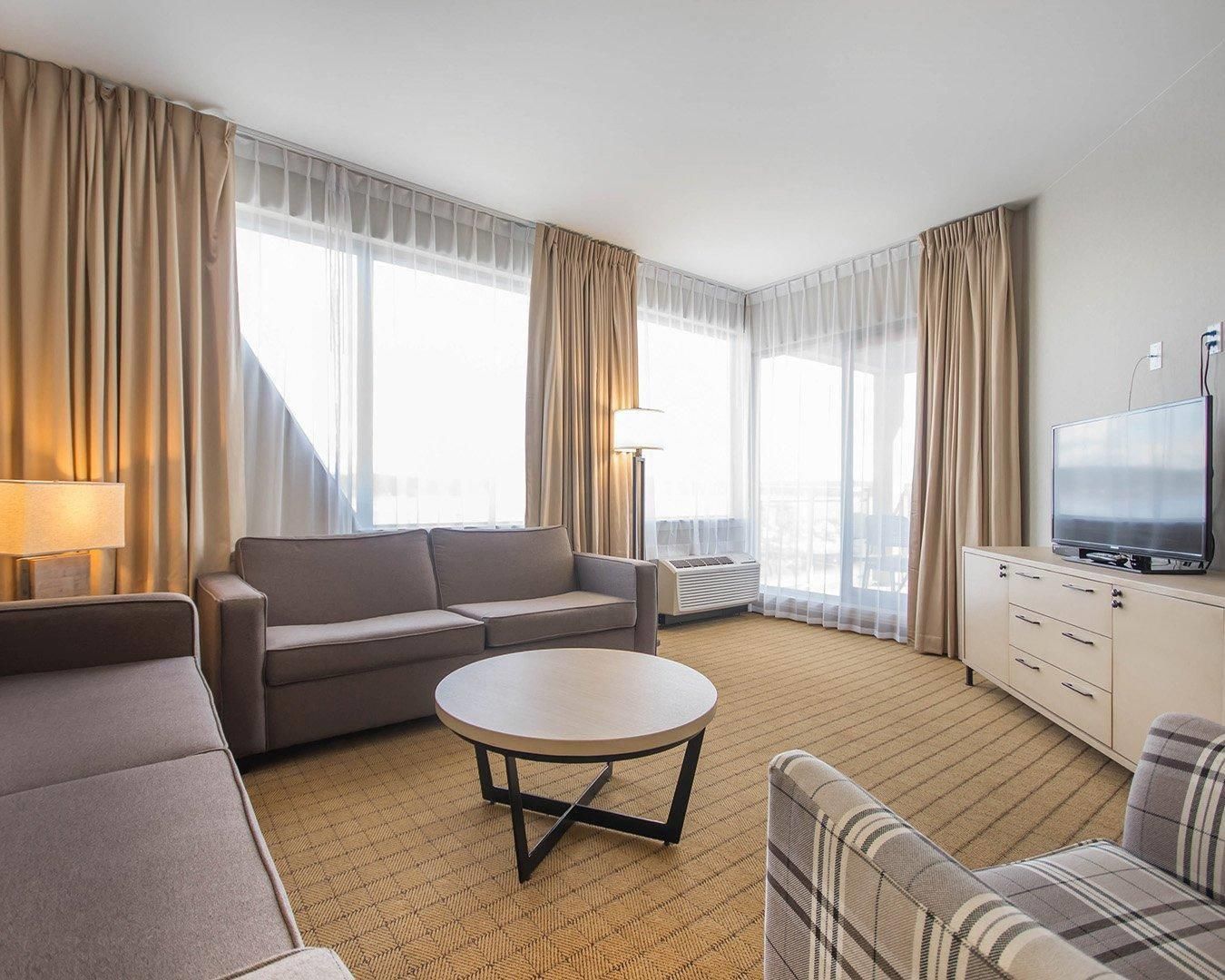 A hotel room with a sofa, a round table, a television, and a window with curtains.