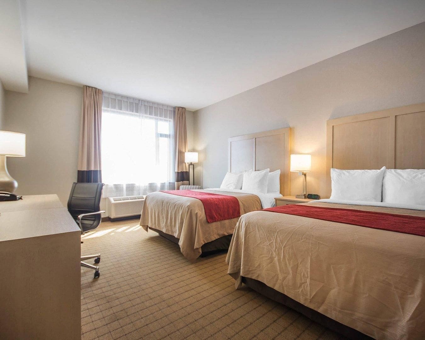 Habitación de hotel con dos camas, un escritorio, una silla y una ventana con cortinas.