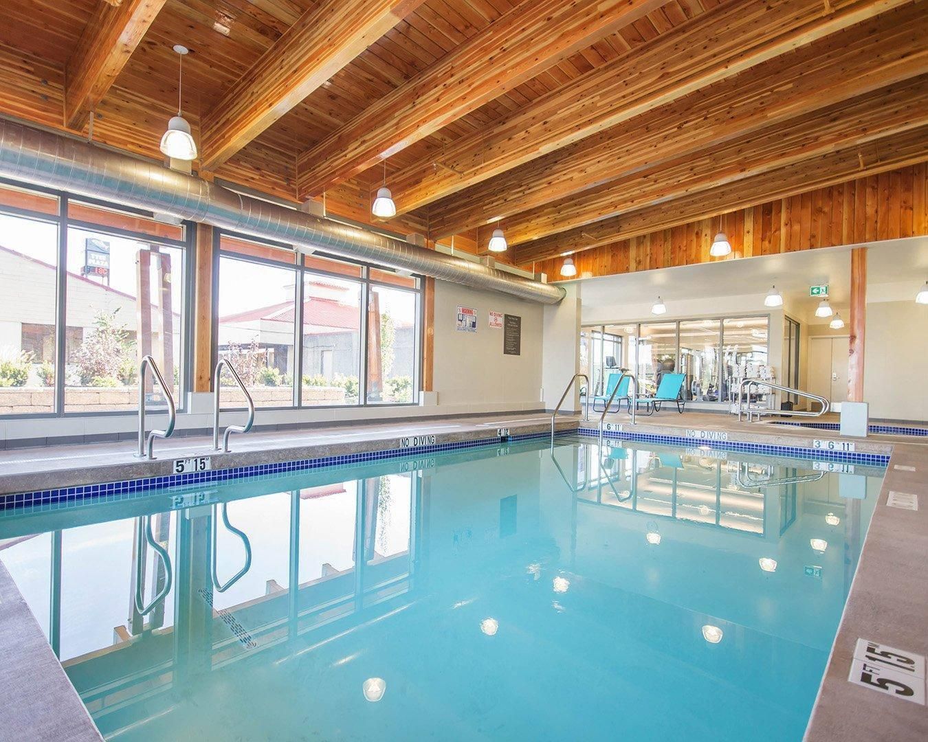 An indoor swimming pool with wooden beams, clear glass walls, and a no diving sign.