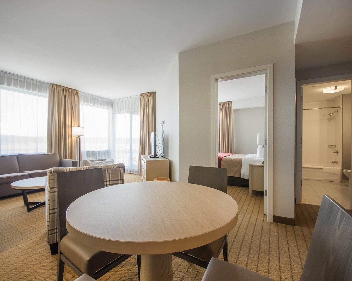 A hotel room with a round dining table, a sofa, a bed, and a bathroom visible through an open door.