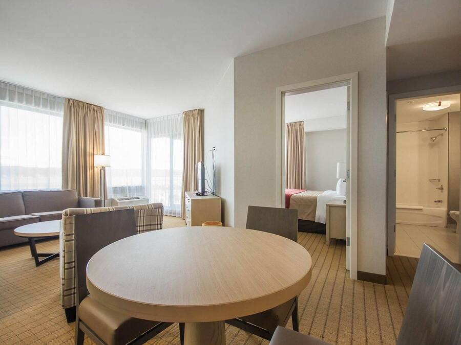 A hotel room with a round dining table, a sofa, a bed, and a bathroom visible through an open door.