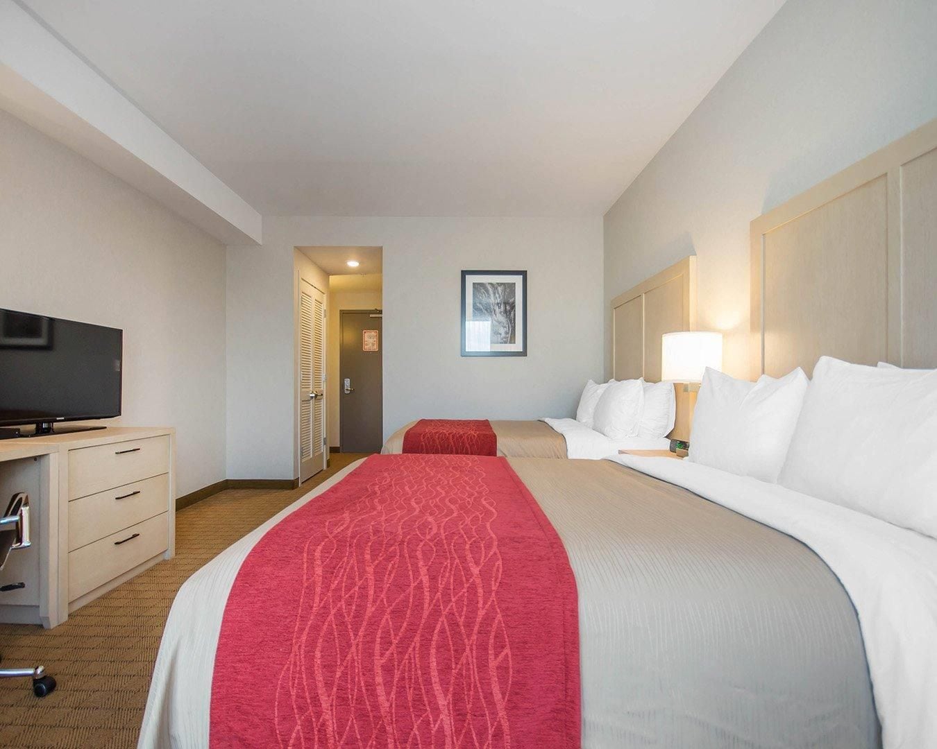 Una habitación de hotel con cama, escritorio con televisor, lámpara y puerta que da a otra habitación.
