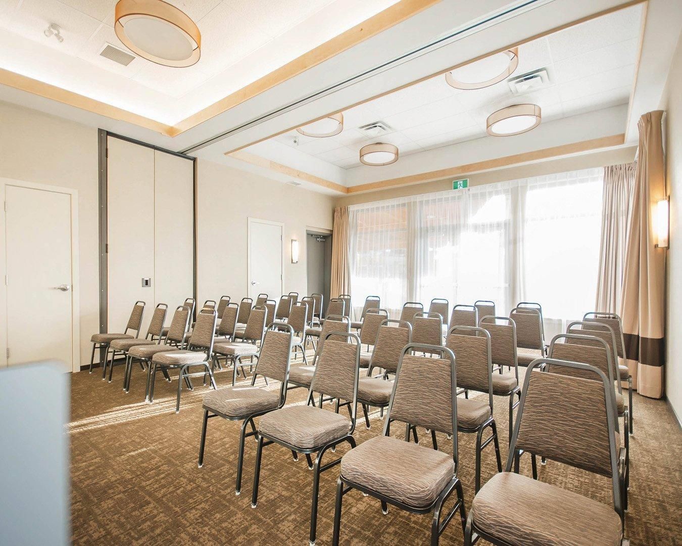 A conference room with rows of chairs, a carpeted floor, and a large window with curtains.