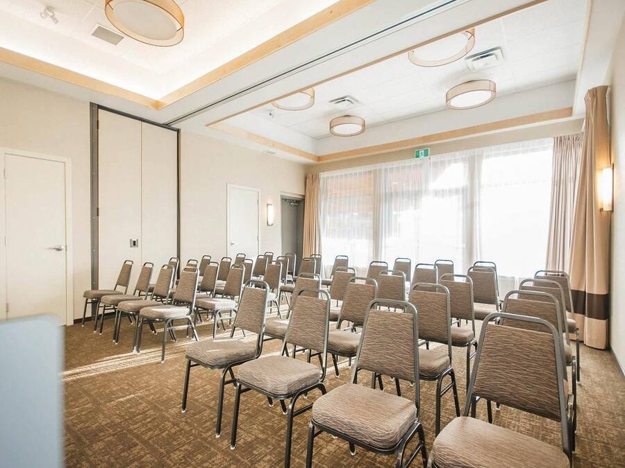 A conference room with rows of chairs, a carpeted floor, and a large window with curtains.