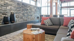 Un interior moderno con pared de piedra, vigas de madera en el techo y una zona de estar con sofá y mesa de centro.