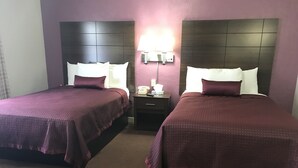 Habitación de hotel con dos camas, cada una con cabecera, mesita de noche con lámpara y teléfono.