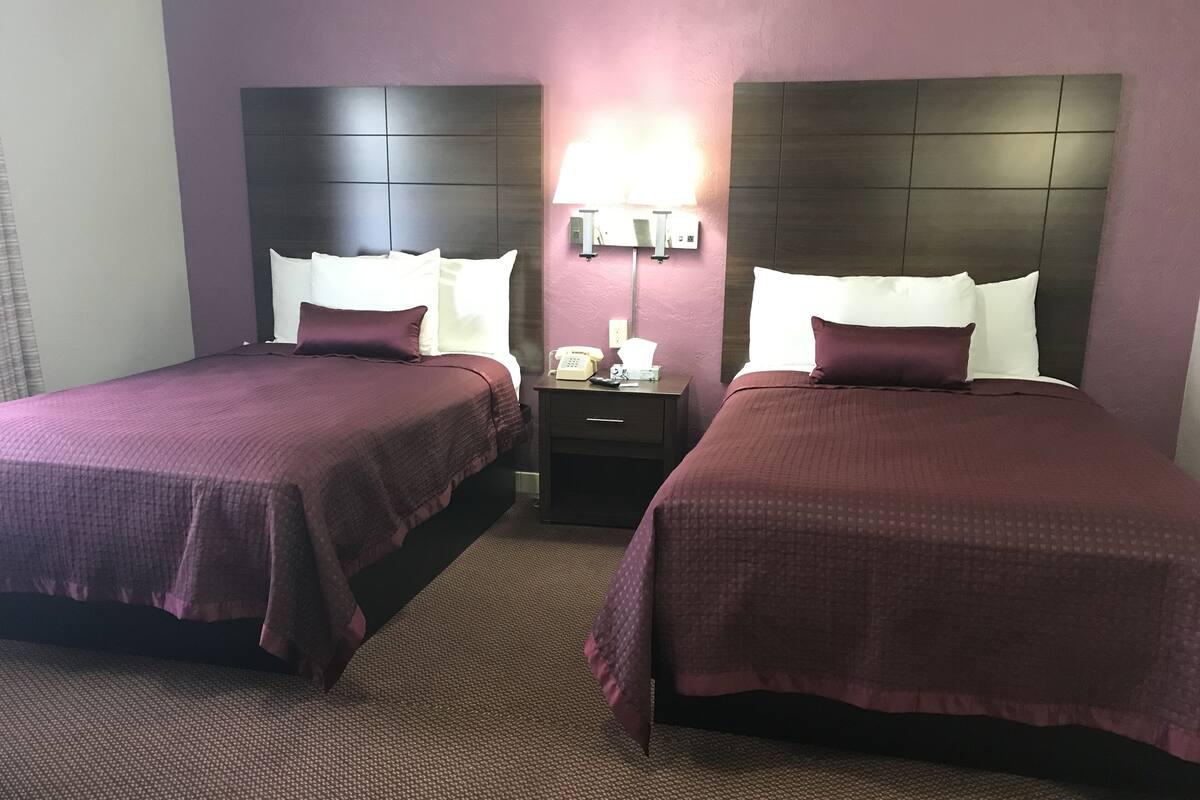 A hotel room with two beds, each with a headboard, a nightstand with a lamp, and a telephone.