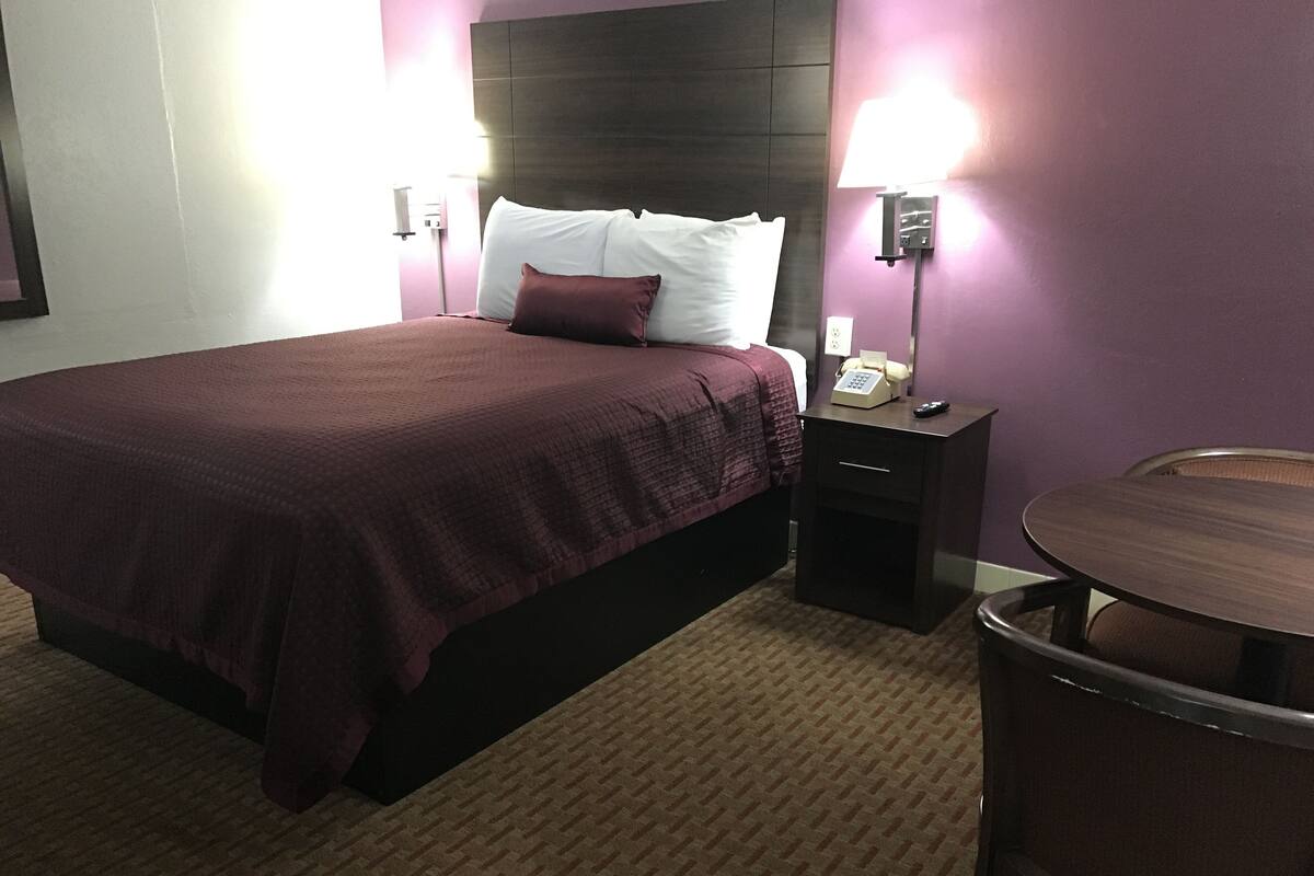 A hotel room with a bed, bedside table, lamp, and a small round table.