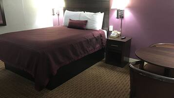 A hotel room with a bed, bedside table, lamp, and a small round table.