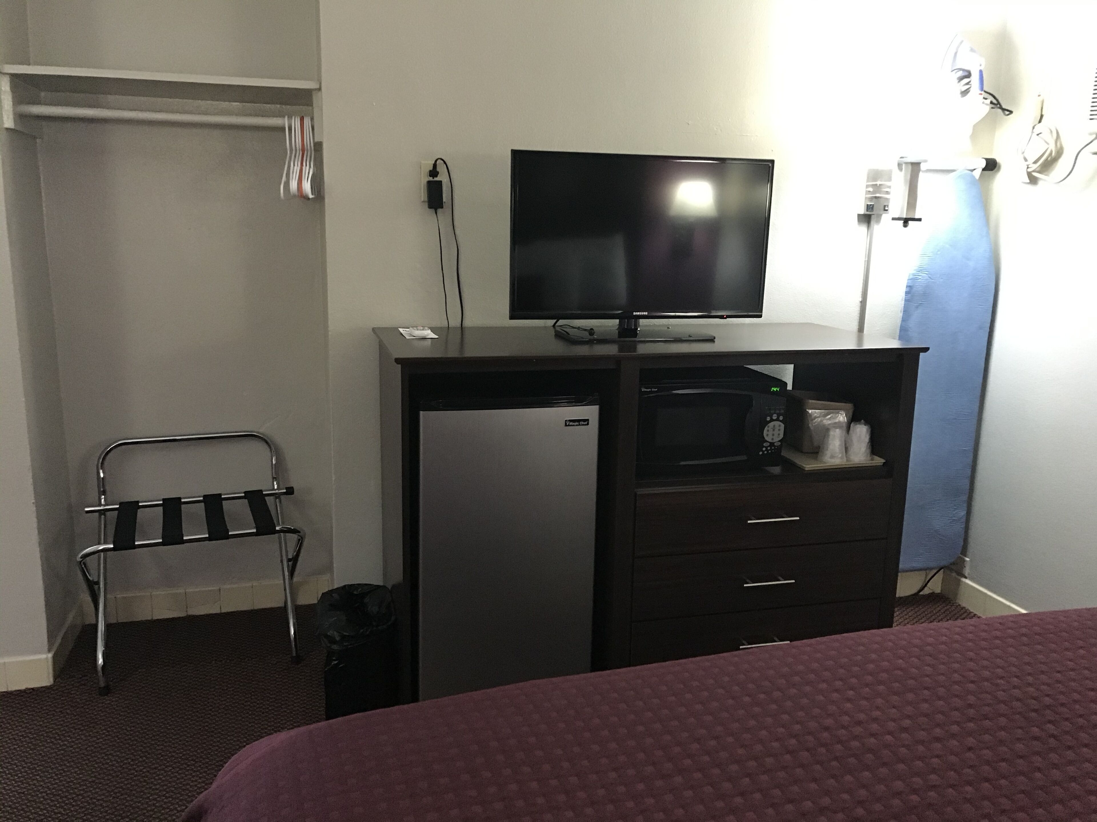 A hotel room with a bed, a desk with a television, a microwave, and a small refrigerator.