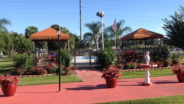 Un parque con senderos rojos, plantas en macetas y una estatua.