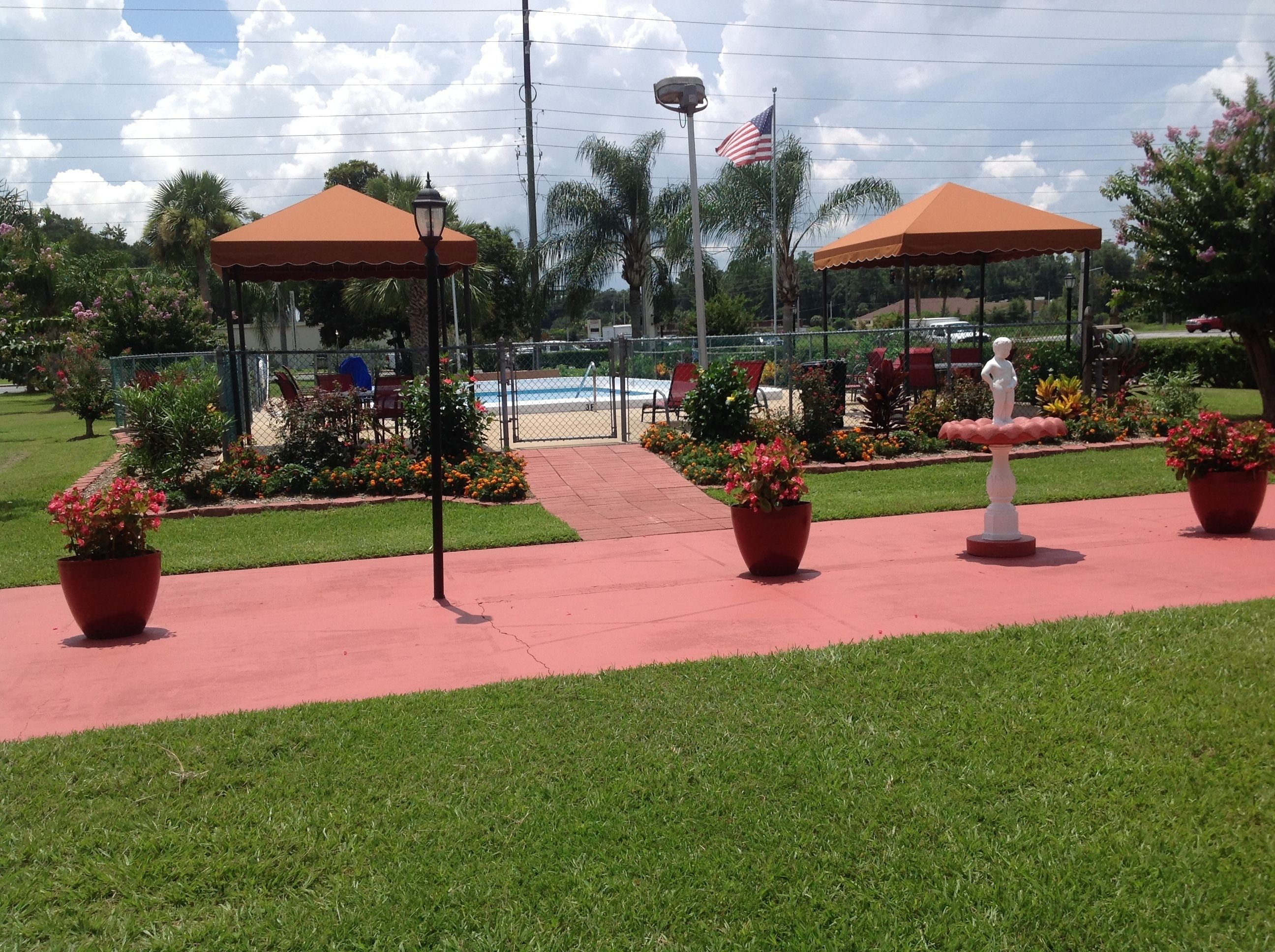 Un jardín con dos pabellones de techo rojo, una estatua y una piscina al fondo.