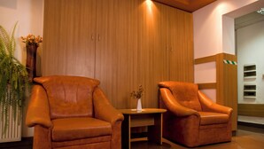 Two leather armchairs, a wooden table, and a vase with flowers in a corner of a room with wooden paneling and a white wall. - Est Hotel Bucharest (Bucharest)