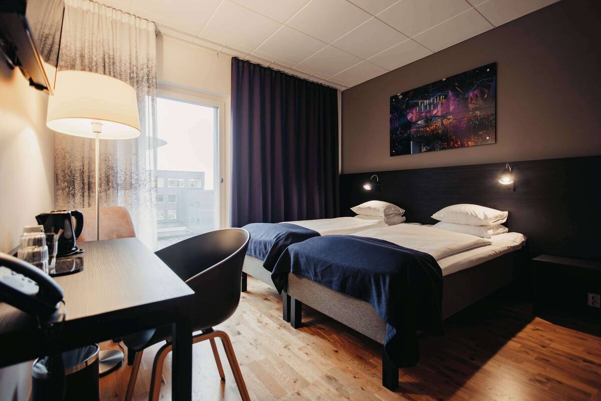 Une chambre d’hôtel avec un lit, un bureau, une chaise, une machine à café et un tableau au mur.