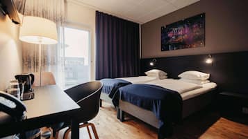 Een hotelkamer met een bed, een bureau, een stoel, een koffiezetapparaat en een schilderij aan de muur.