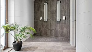Un baño moderno con baldosas grises, una planta en maceta y dos fuentes de agua verticales.