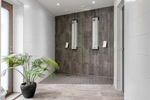 Un baño moderno con baldosas grises, una planta en maceta y dos fuentes de agua verticales.