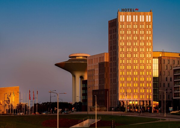 A hotel with a modern design, featuring a prominent tower and a rectangular building with illuminated windows.