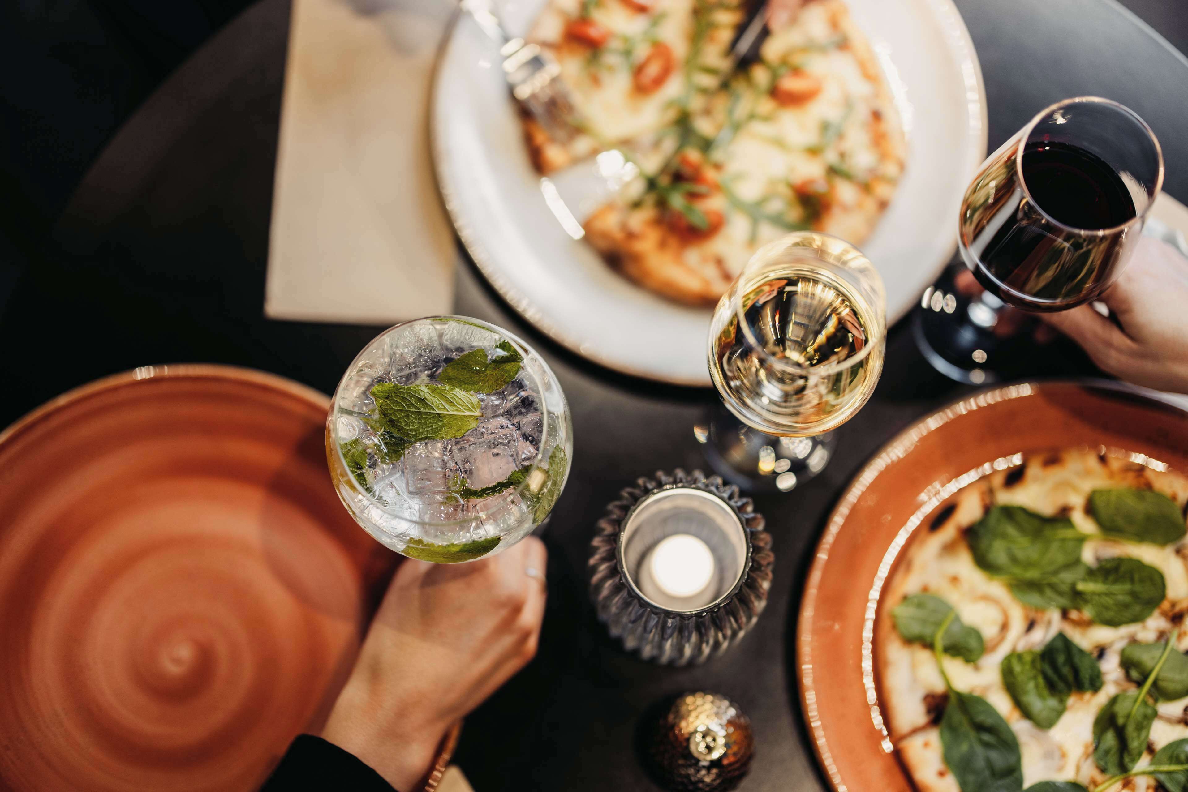 A dining table with a pizza, two glasses of wine, and a decorative candle.