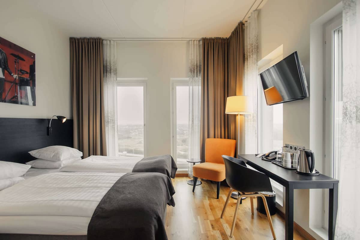 Une chambre d’hôtel avec deux lits, un bureau avec une chaise, un téléviseur à écran plat et une fenêtre avec des rideaux.