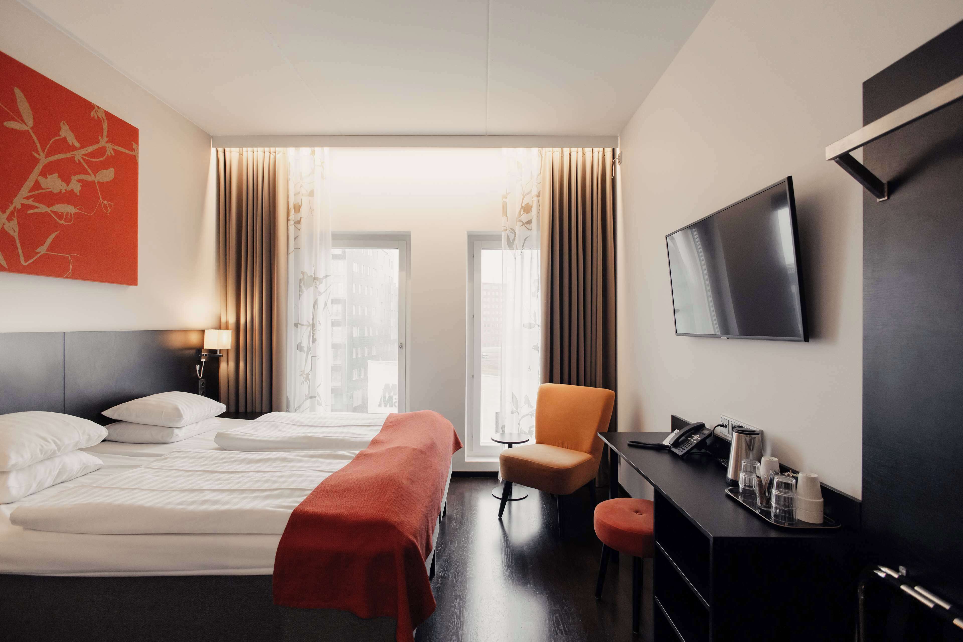 Habitación de hotel con cama, escritorio, silla, televisión y ventana con cortinas.