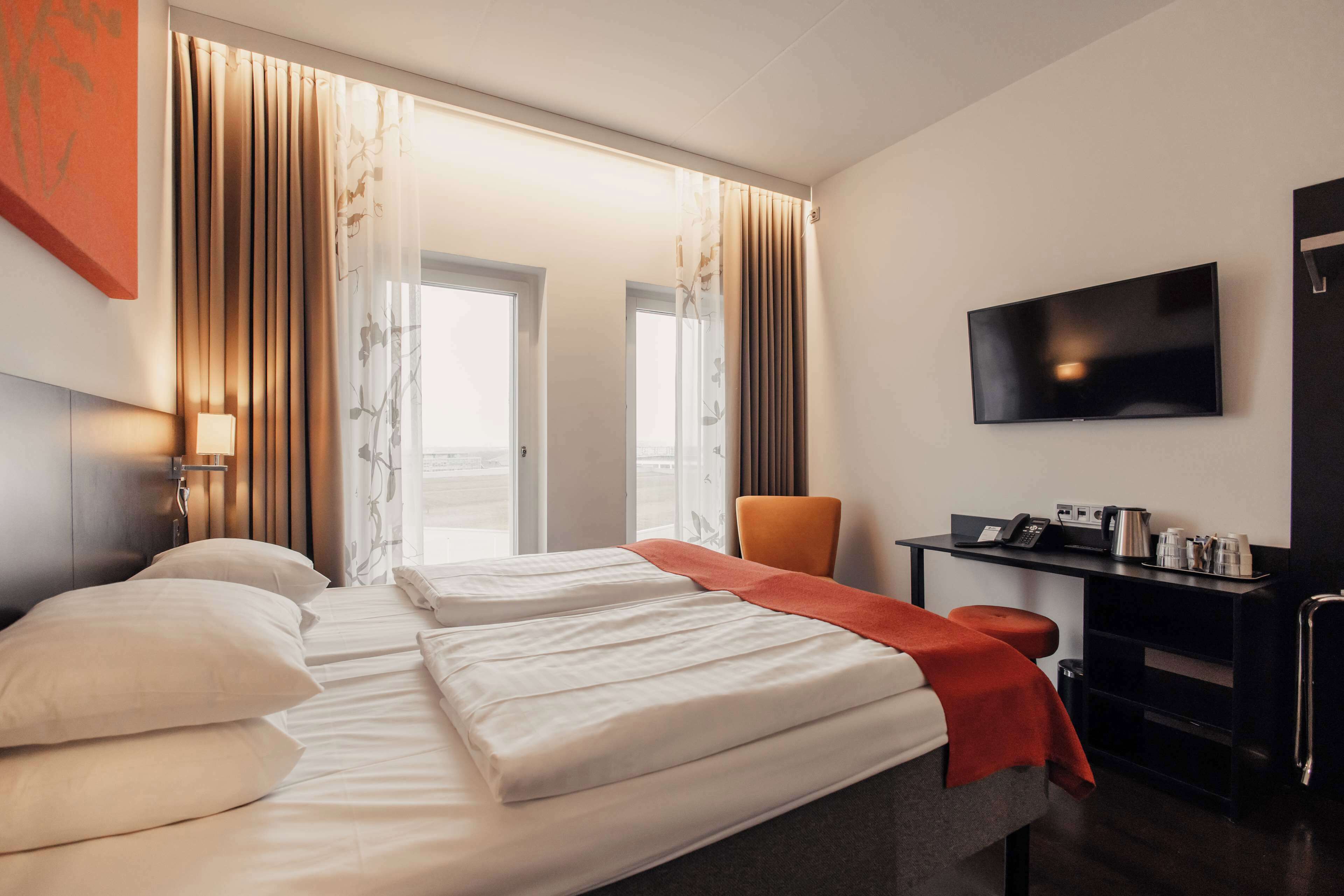 Ein Hotelzimmer mit zwei Betten, einem Schreibtisch mit Fernseher und Blick ins Freie.
