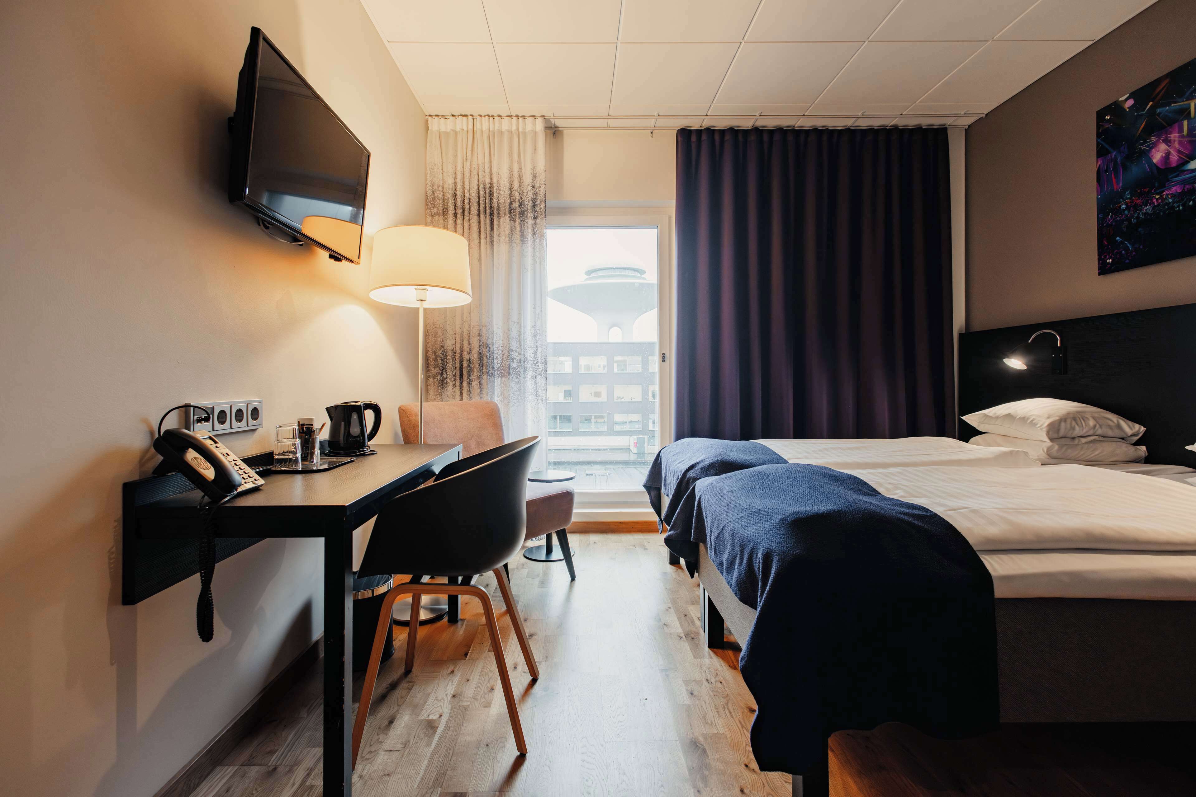 A hotel room with a desk, chair, bed, and a TV mounted on the wall.