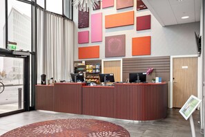 A reception area with a modern design, featuring a red reception desk, a digital information kiosk, and a variety of wall art.