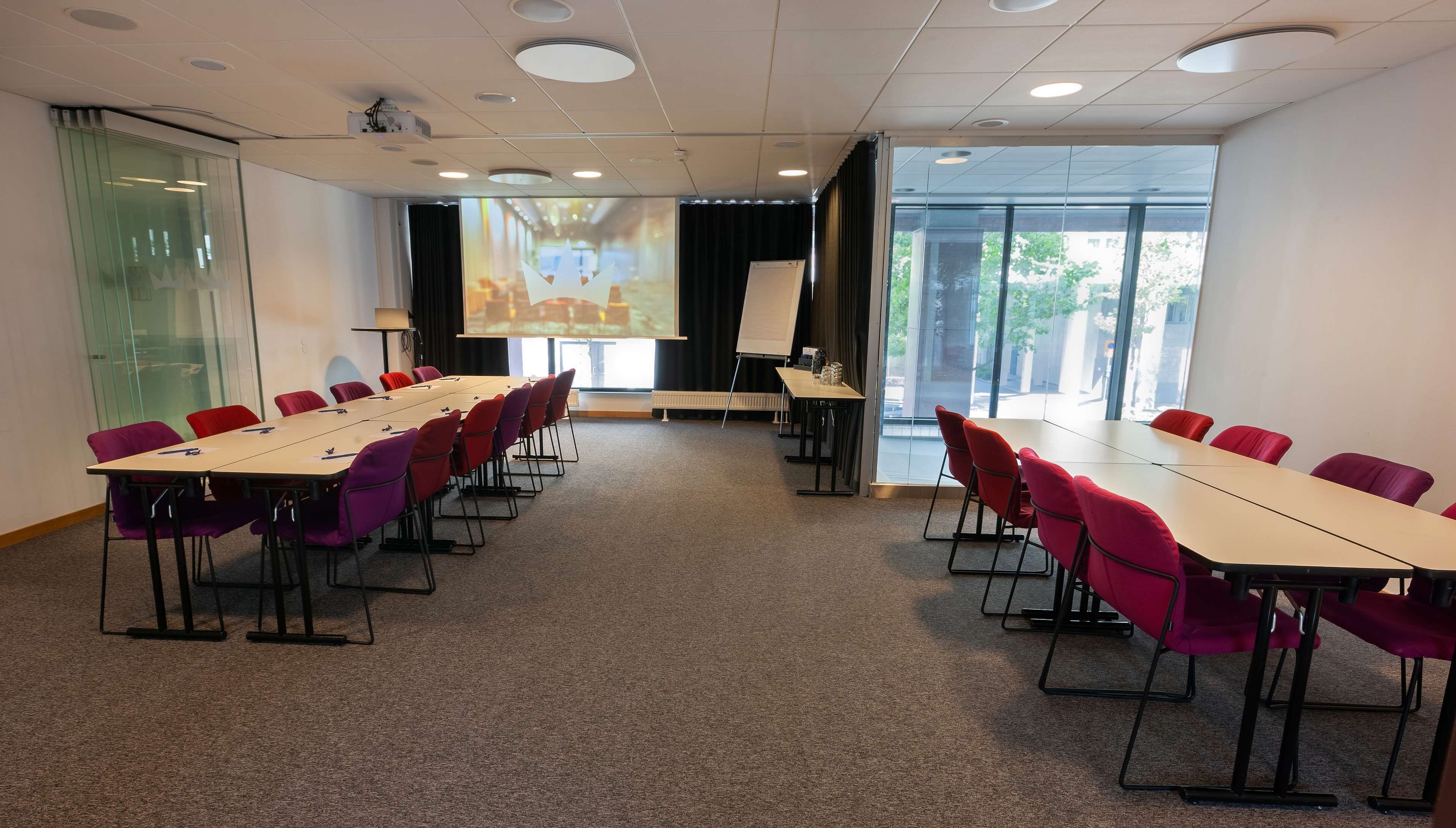 A conference room with a long table, chairs, a projector, and a presentation screen.