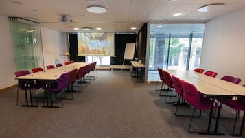 A conference room with a long table, chairs, a projector, and a presentation screen.