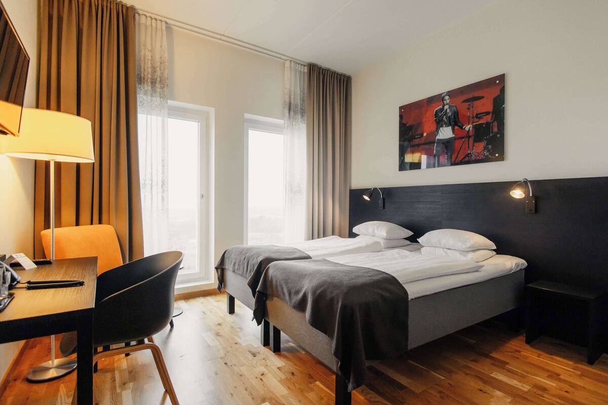 Une chambre d’hôtel avec deux lits, un bureau, une chaise et un tableau au mur.