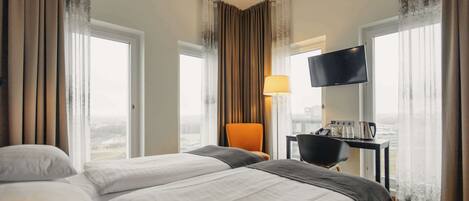 A hotel room with two beds, a desk with a TV, and a view of the city.