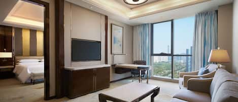 A hotel room with a bed, a desk, a sofa, a TV, and a large window with a city view.