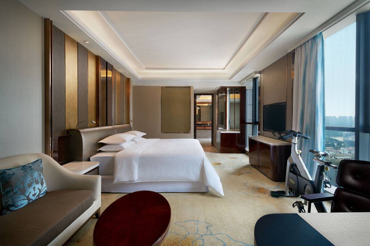 Habitación de hotel con una cama grande, un sofá, un escritorio, un televisor y vistas a la ciudad.