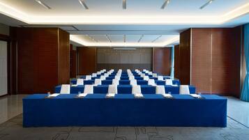Una sala conferenze con un lungo tavolo coperto da una tovaglia blu, dotata di sedie bianche e bicchieri.