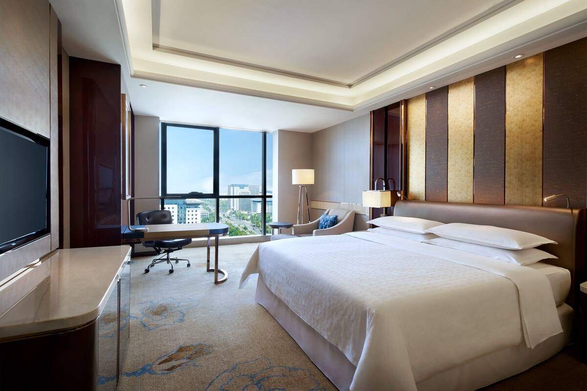 Habitación de hotel con una cama grande, un escritorio, una silla, un televisor y vistas de la ciudad.