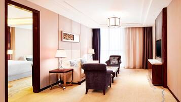 A hotel room with a bed, a sofa, a chair, a small table, a lamp, a TV, and a large mirror.